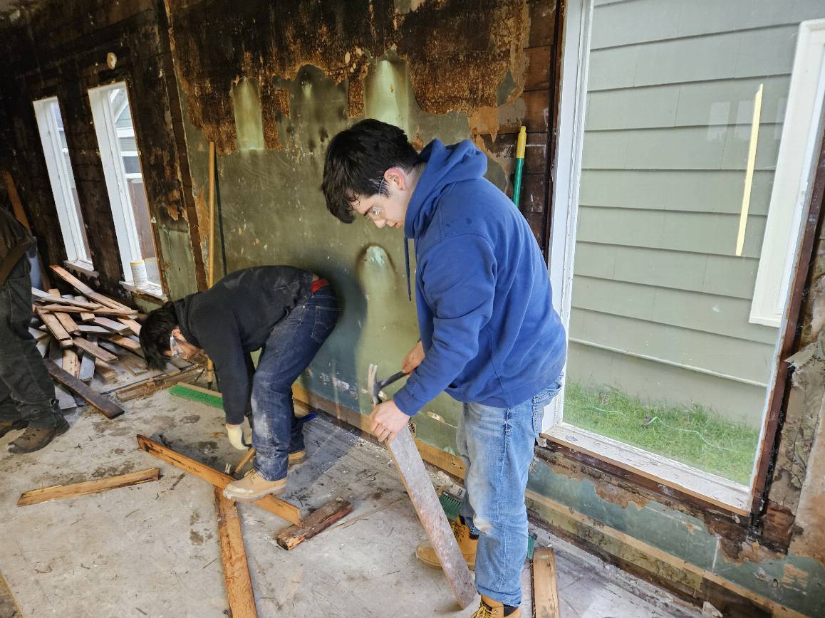 Juan Santillano and Saul Ordonez, Construction pre-Apprenticeship Program (CAP) students with the Advanced Manufacturing Skills Center (AMSC) of Edmonds College, pull up old floorboard as part of their volunteer demo work with Housing for Humanity of Snohomish County. (photo credit: Edmonds College).