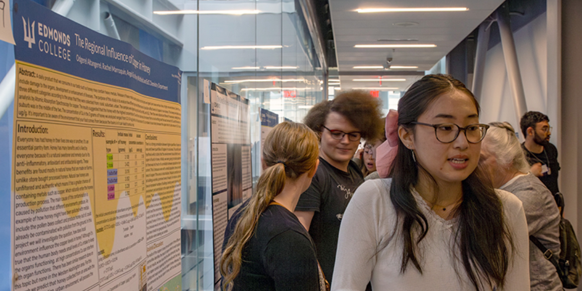 The 2026 National Conference on Undergraduate Research posters hung in a hallway with students passing by featuring a research poster created by an Edmonds College Student.
