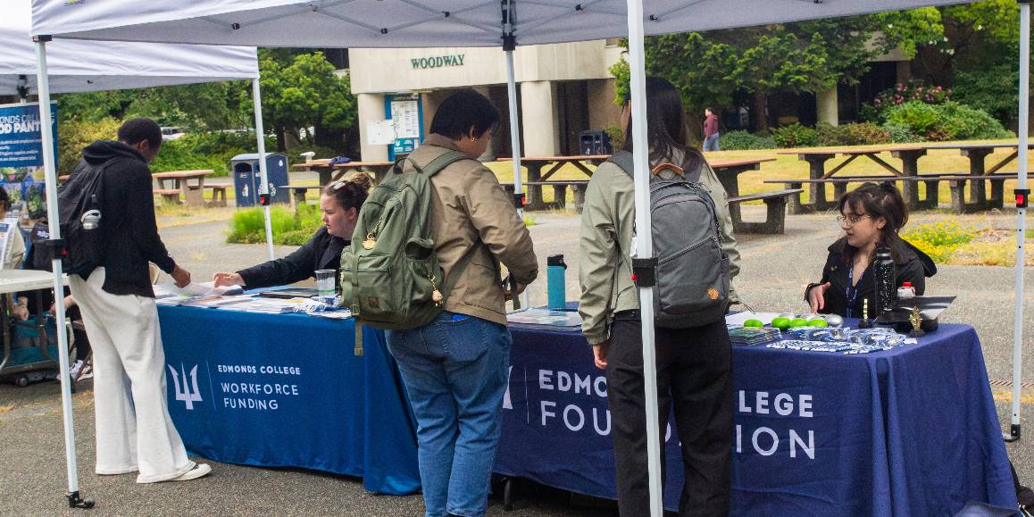 Three students checking out the resource fair tabling options under white tents at the Edmonds College Triton Visit Day event in 2025