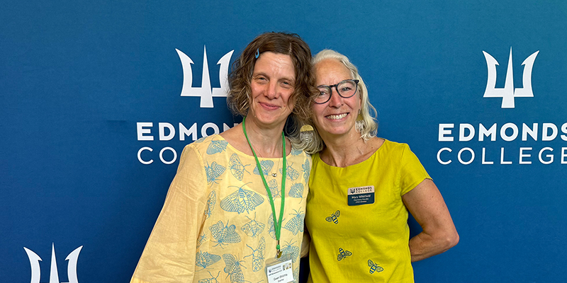 Faculty Mentors, Gwen Shlichta and Mary Whitfield smile together in front of an Edmonds College background. Faculty Mentors, Gwen Shlichta and Mary Whitfield smile together in front of an Edmonds College background.
