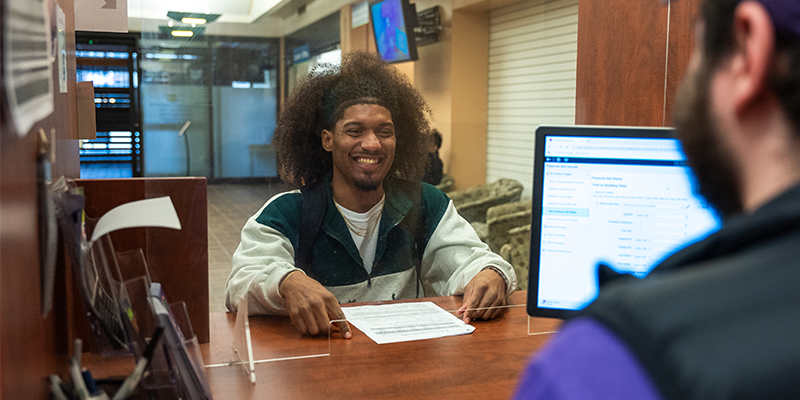 A student at a reception desk talking to someone who has a computer screen open. A student at a reception desk talking to someone who has a computer screen open.