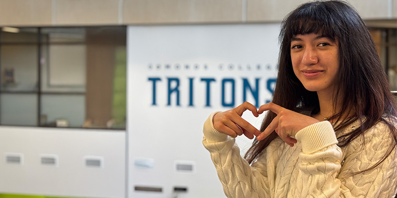 Katelyn Thomas poses with heart hands in front of Edmonds College Tritons Sign