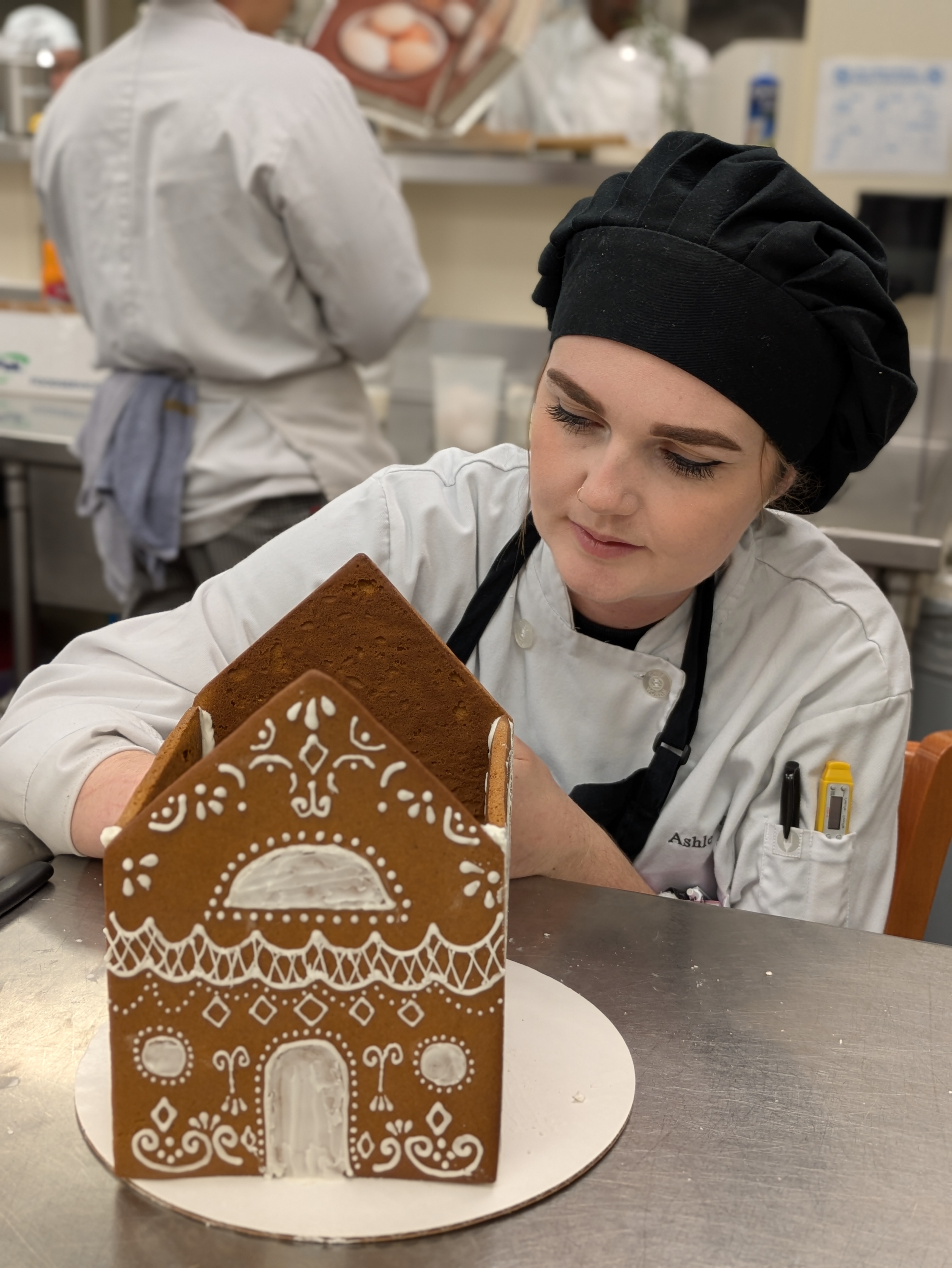Student putting the final touches on a gingerbread house for the Holiday Luncheon