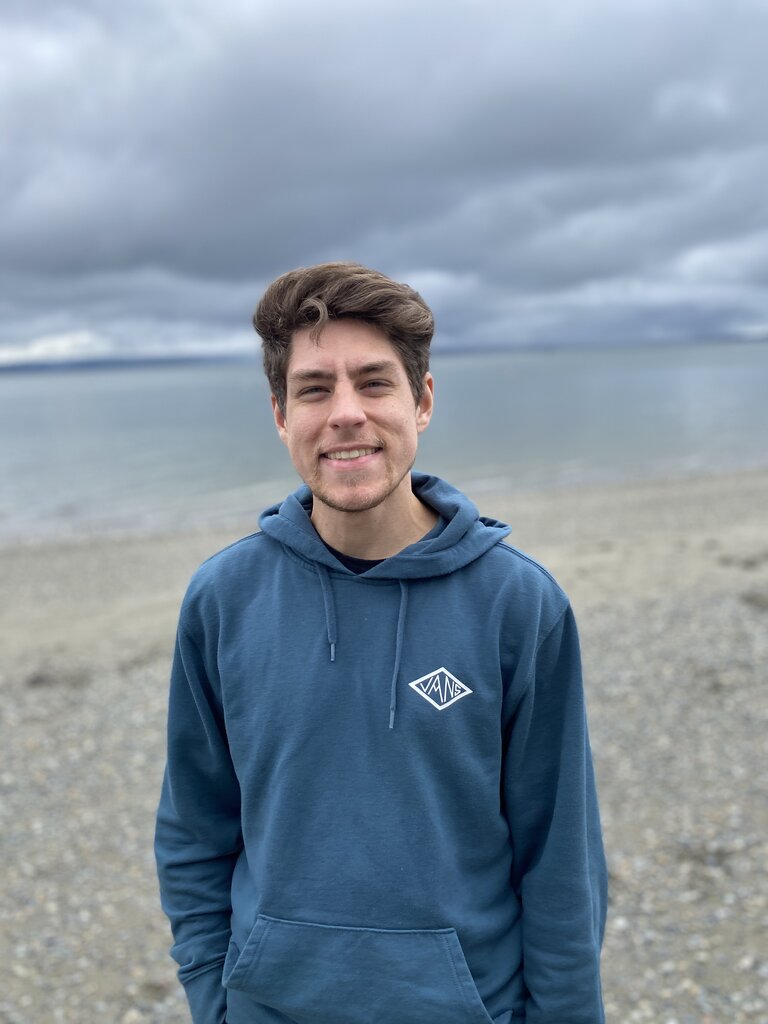 Photo of young white man in blue sweatshirt at beach. Student featured is Joseph Oberhausen