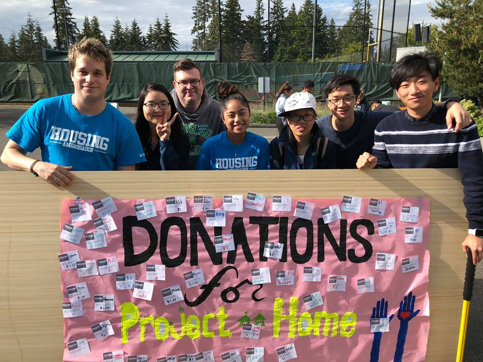 Housing Ambassadors and Project Home team members holding a donations board at an event.