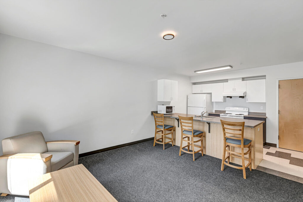 Minimal living room with two armchairs, small coffee table, carpet flooring, and large window.