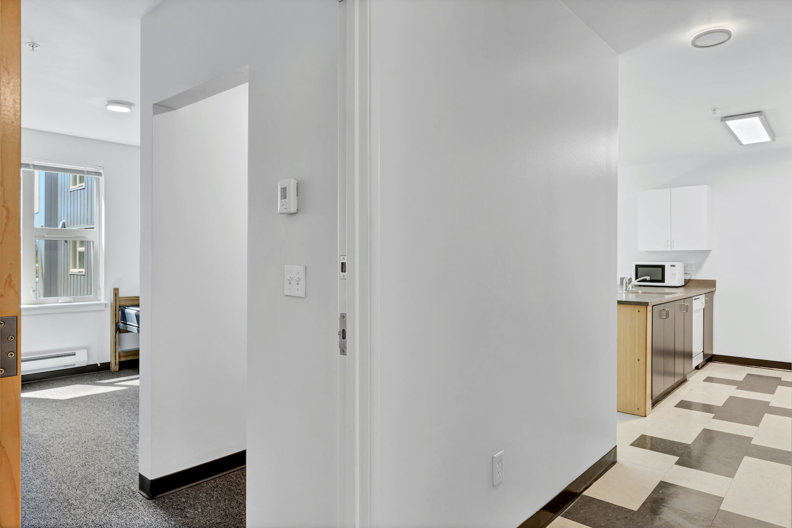 Hallway leading to bedroom and kitchen, with white walls and visible doorways.
