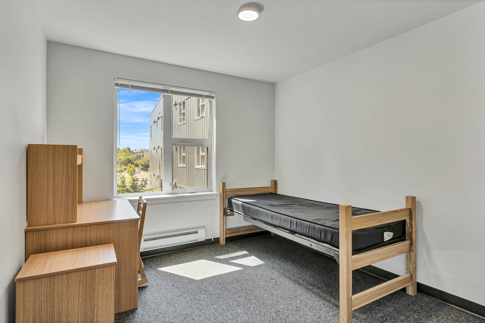 Bedroom with single bed, wooden desk setup, and window with natural light.