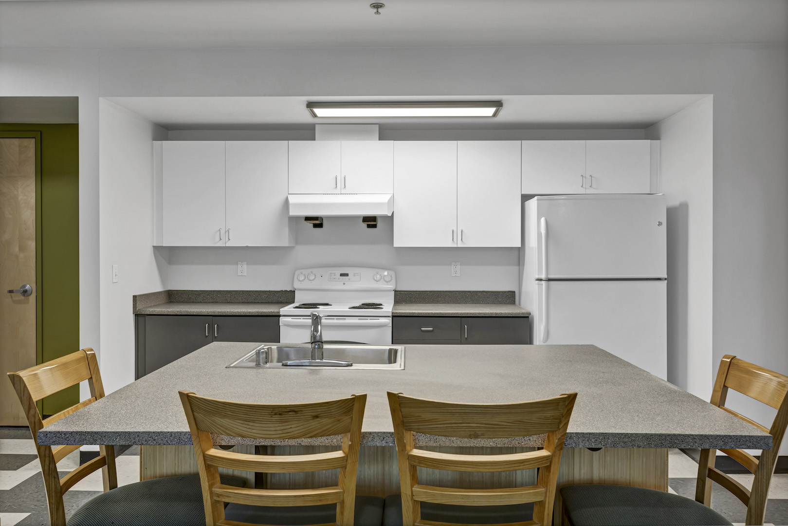 Front-facing view of kitchen with island sink, white cabinets, stove, and refrigerator.