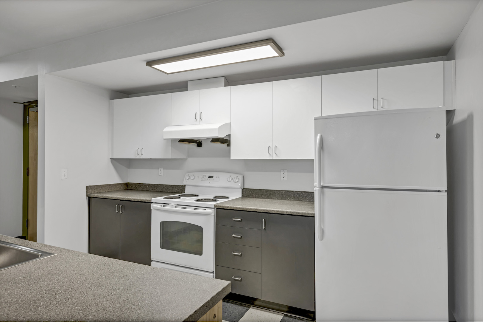 Angled view of kitchen showing stove, refrigerator, white cabinetry, and countertop space.