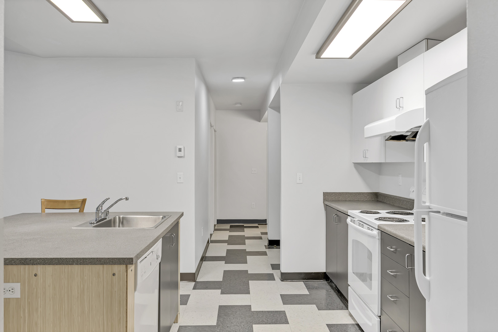 Kitchen area leading into hallway with patterned flooring and visible appliances.