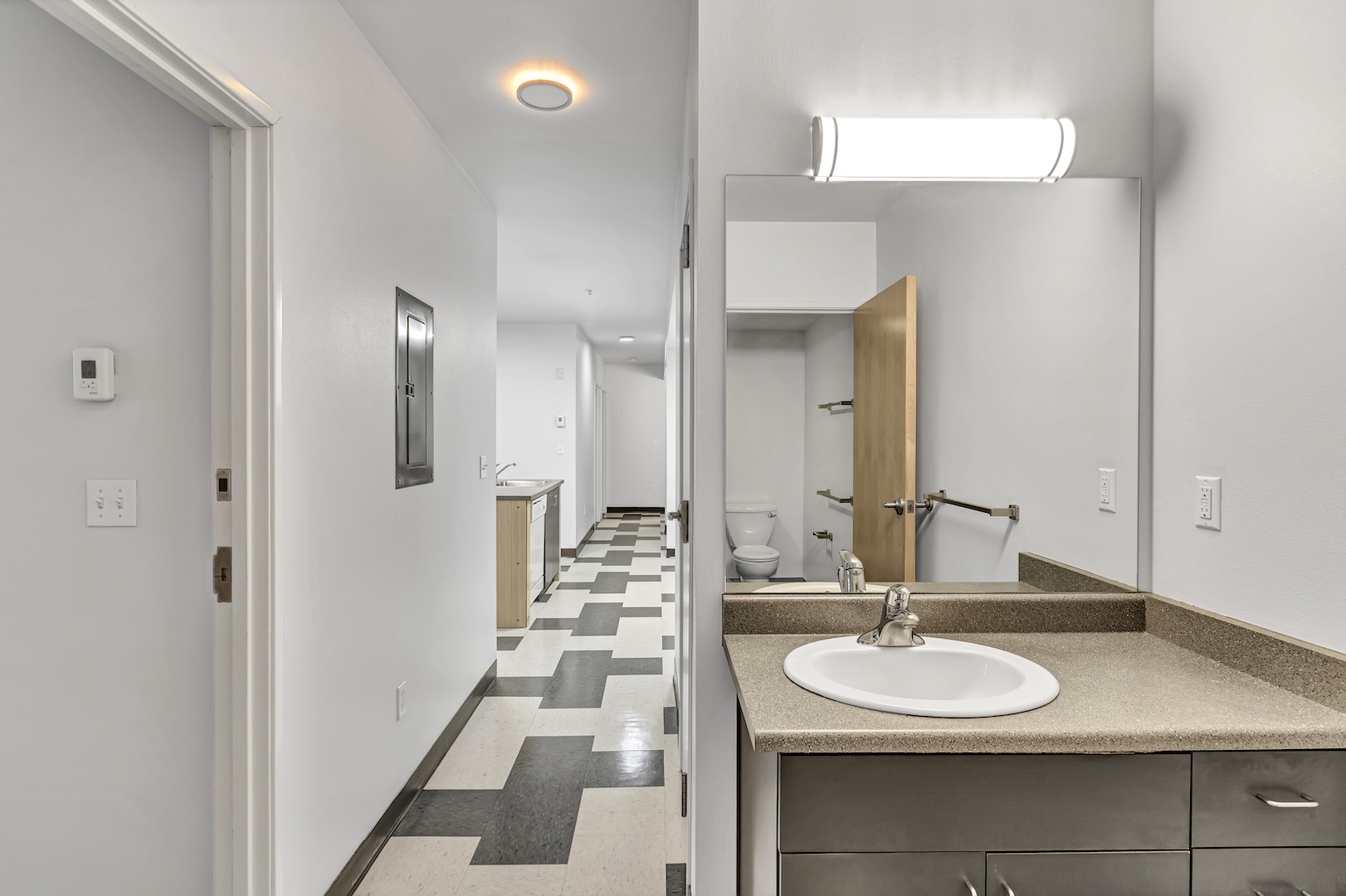 Bathroom sink with mirror and lighting, connected to hallway view toward kitchen.