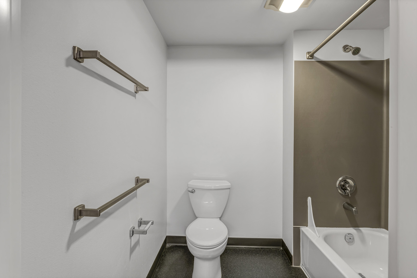 Bathroom with bathtub, shower, toilet, and wall-mounted towel bars.