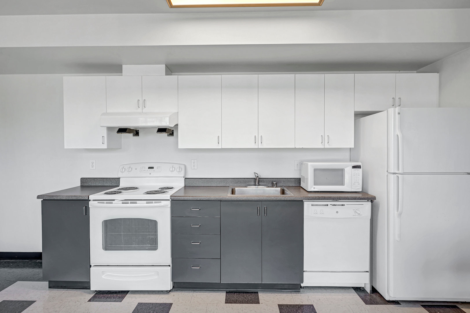 Showing the kitchen area of a studio unit. Equipped with a fridge, oven, stove, and a microwave.