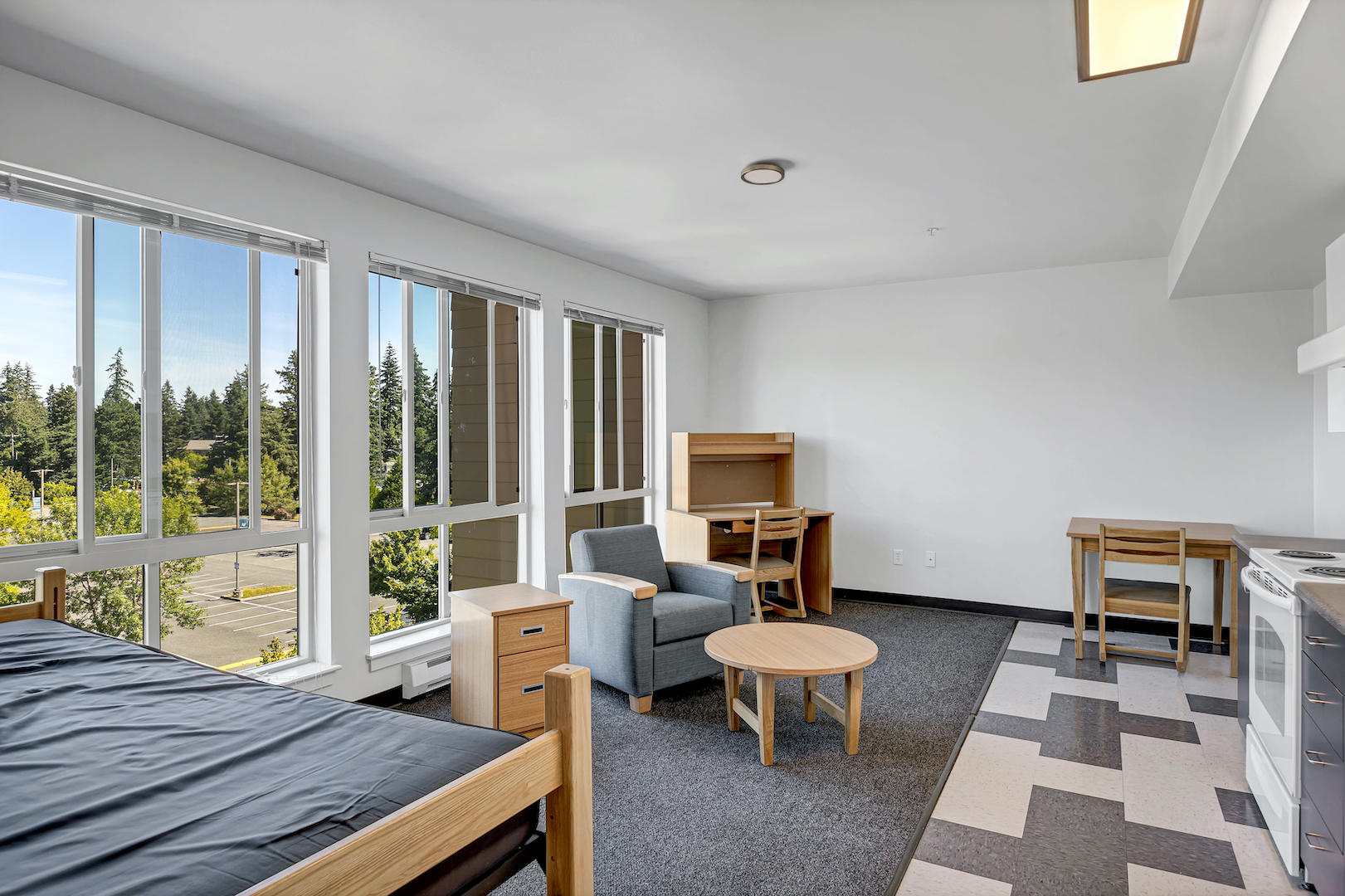Living area of a studio furnished with twin xl bed, study desk, arm chair, and desk chair