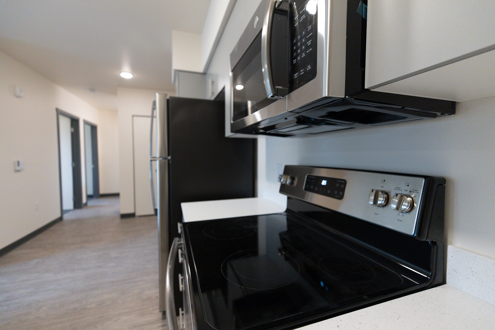 bedroom hallway view from the kitchen area side view of kitchen stove top with a microwave on top and a refrigerator on the side. showing the hallway that has the entry way to the private bedrooms
